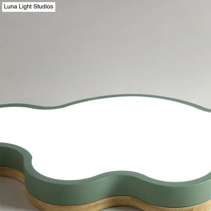 A modern cloud flush mount ceiling lamp with matte sage green frame and warm wood-toned base for kids bedroom