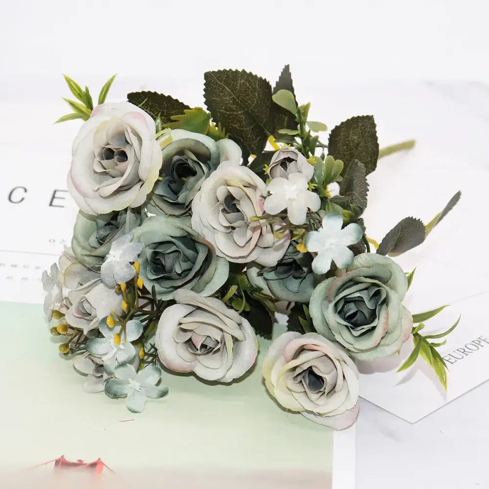 A delicate bouquet of silk fake flowers featuring blue peony and tea rose in soft sage green pale pink and cream hues