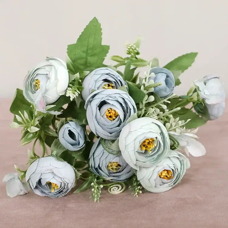 A delicate bouquet of silk fake flowers featuring light blue ranunculus with yellow centers for home garden decor