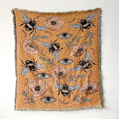 A mustard-yellow decorbites bohemian throw blanket with black-and-white bees pink poppies blue eyes and fringed edges