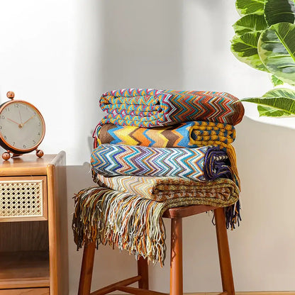Stack of colorful bohemian knit tassel blankets with multicolored zigzag patterns and fringed edges for bedroom decor