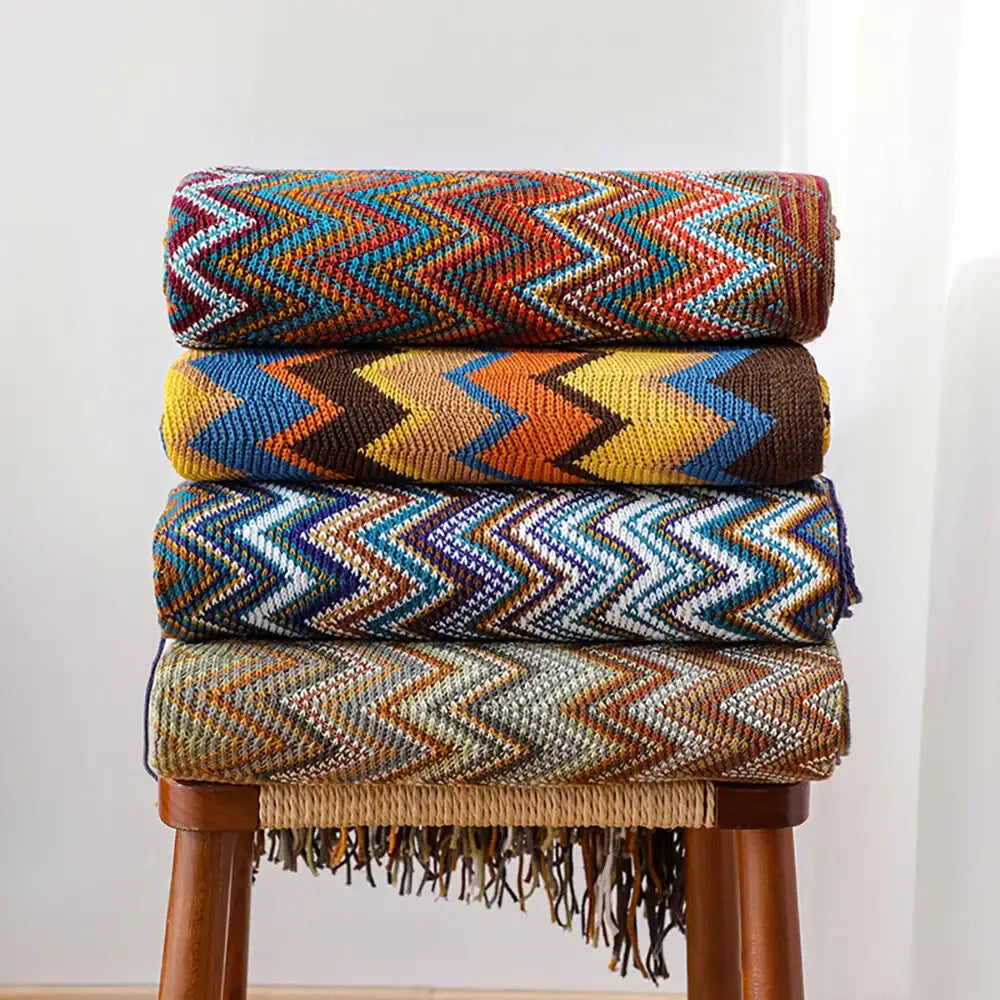 Stacked bohemian knitted blankets with vibrant multicolored zigzag patterns and fringe detailing for living room use