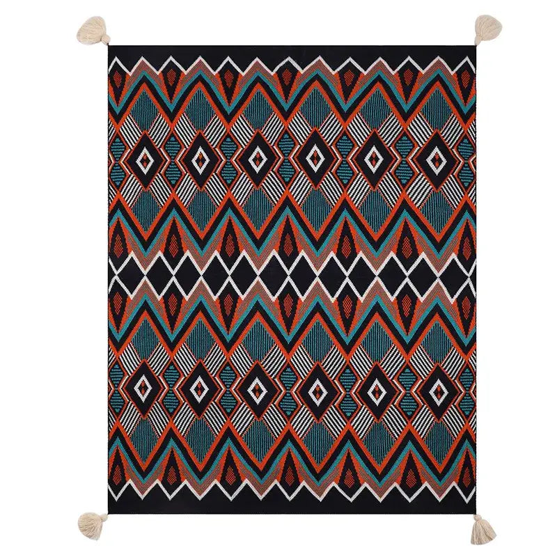A bohemian knitted throw blanket with bold teal orange black and white geometric pattern and cream tassels at corners