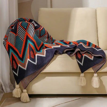 A cozy navy blue bohemian knitted throw blanket with bold teal orange white geometric patterns and cream tassels