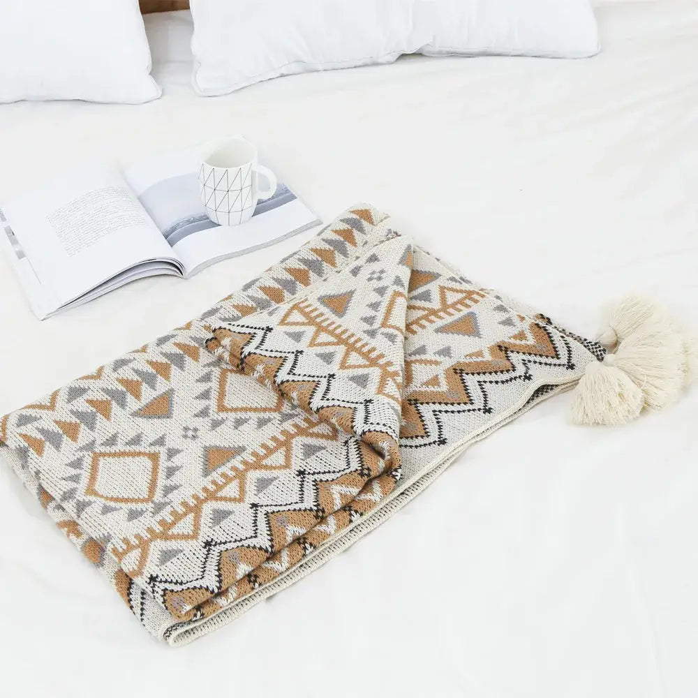 Cozy cream bohemian knitted throw blanket with geometric tan gray and black pattern and tassel accent for bedroom use