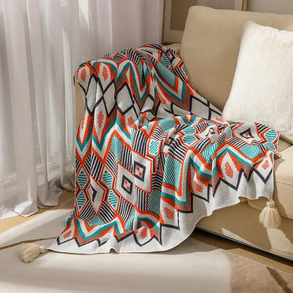 A cozy bohemian knitted throw blanket with bold orange teal black and white geometric pattern and tassels