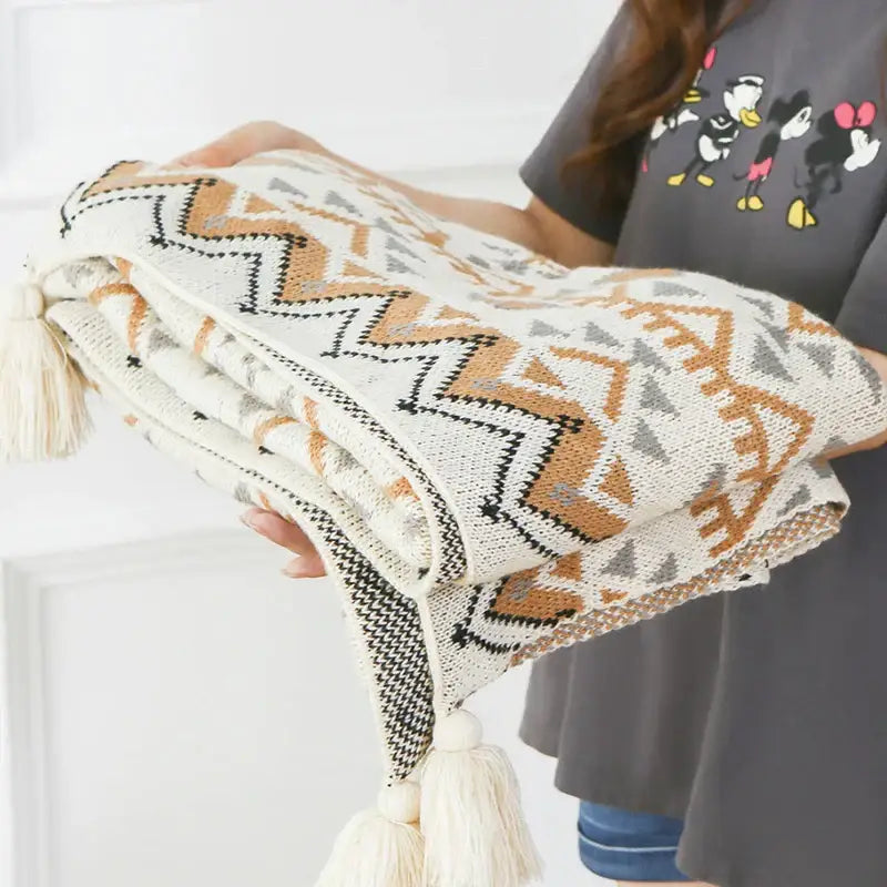 A cozy cream bohemian knitted throw blanket with tan black gray geometric pattern and decorative tassels at each corner