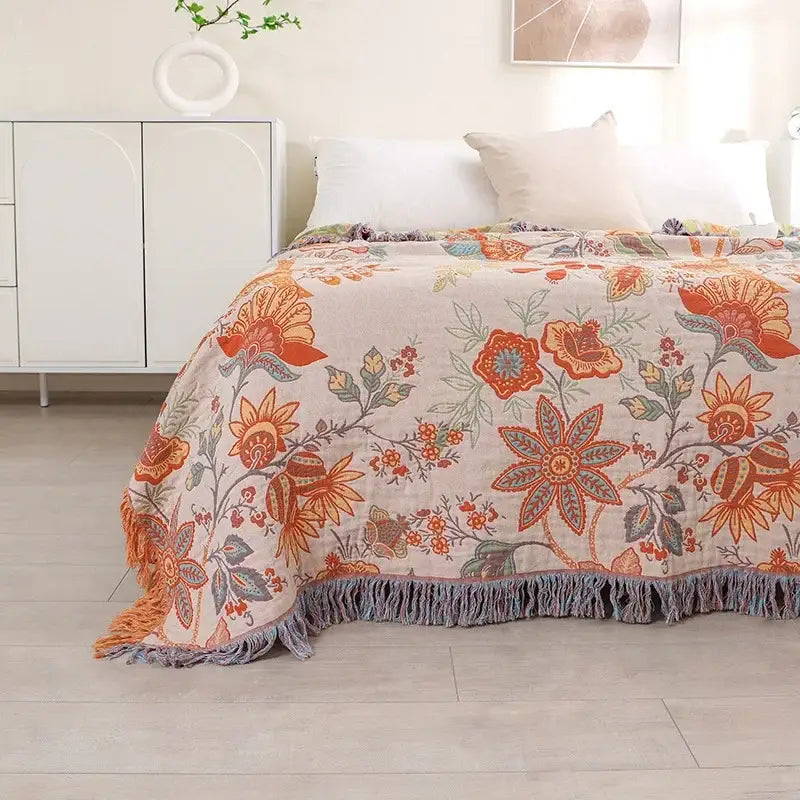 A cozy beige bohemian sofa blanket with vibrant orange and green floral patterns and soft fringe by decorbites
