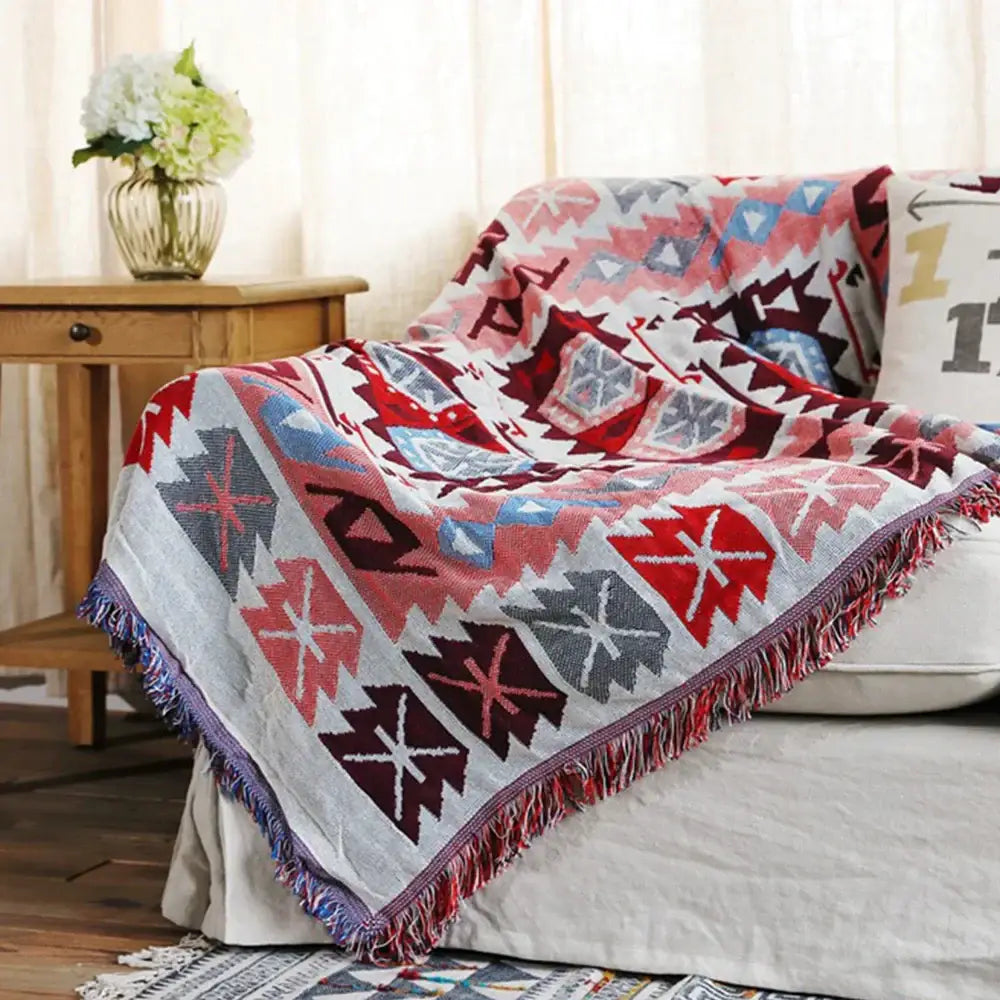A cozy bohemian pink and red knitted cotton throw blanket with vibrant geometric pattern and fringed edges for decorbites decor