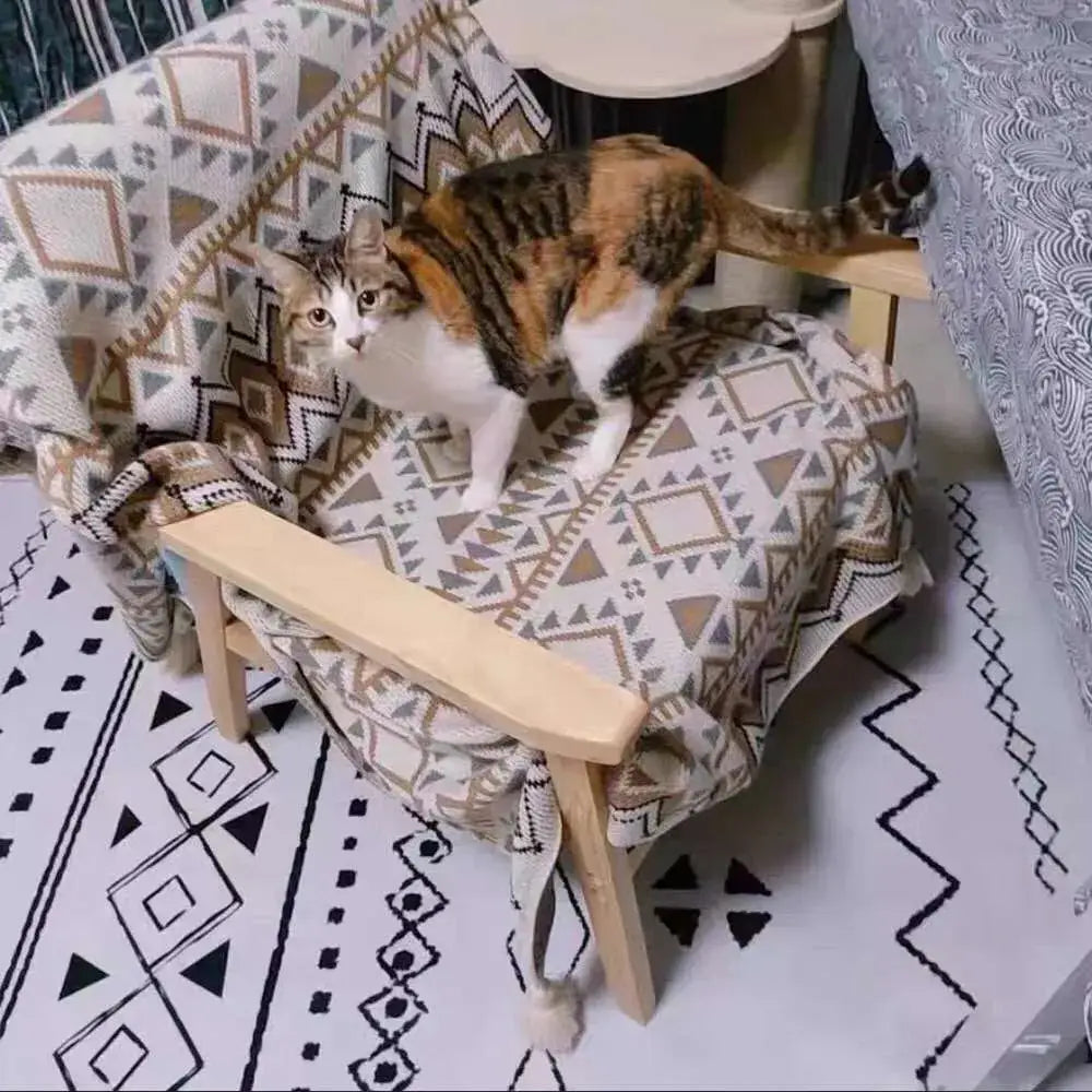 A calico cat stands on a chair draped with a decorbites bohemian tassel knit geometric tapestry throw