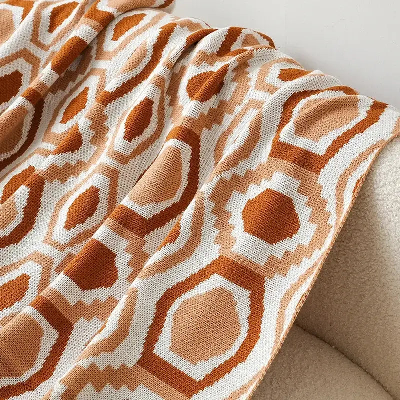 A cozy bohemian winter blanket knitted with orange and white geometric patterns for bedroom decor by decorbites