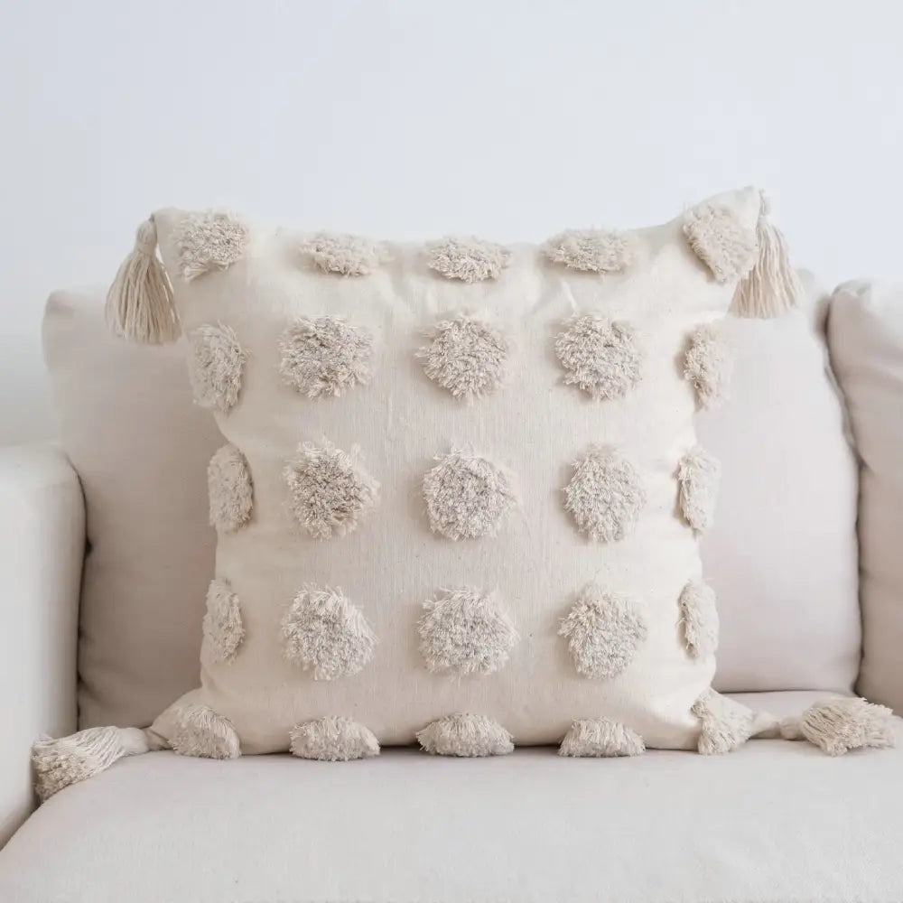 Cream-colored tufted tassel cushion cover with textured woven fabric and fluffy pom-poms for living room decor