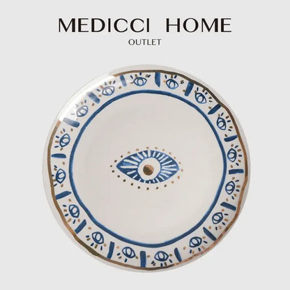 A white ceramic boho bright eyes ceramic dinner plate with blue and gold eye motifs from medicci home decorbites bright eyes