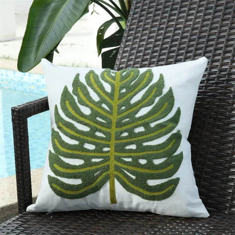 White cushion featuring a textured, embroidered monstera leaf in shades of green and yellow.