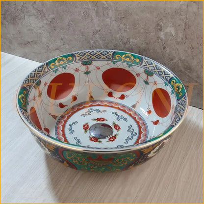 A decorbites boho retro ceramic bathroom sink with intricate red green and gold floral bird patterns around a metallic drain