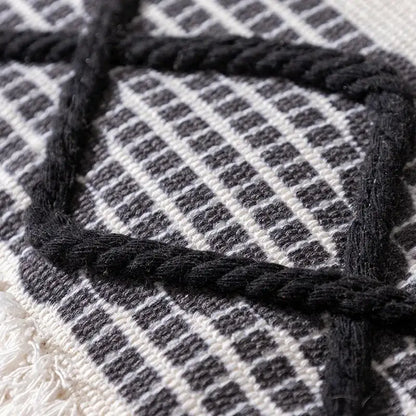Black braided rope detail woven over textured white and gray checkered fabric on boho tufted fringed black pillowcase decorbites