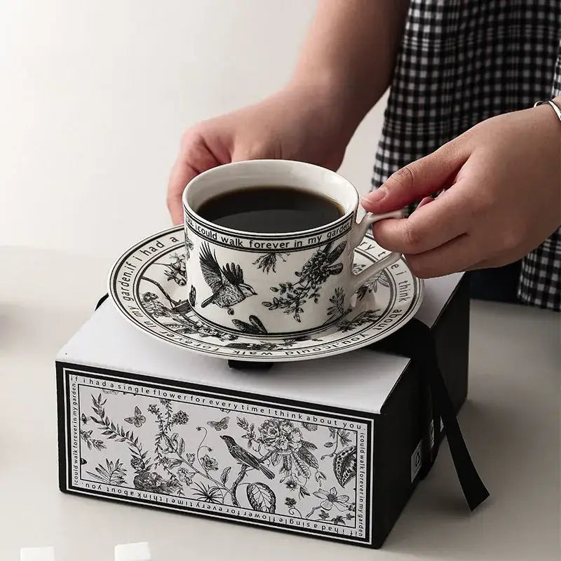 White ceramic bird ceramic coffee cup with black bird and floral design held above matching decorbites black bird saucer