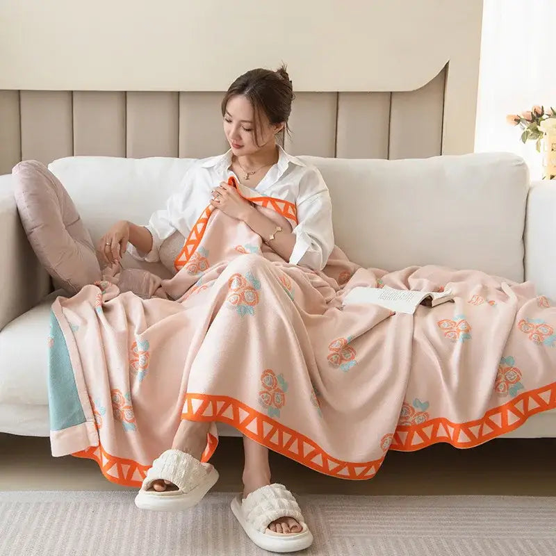 A soft peach summer quilt with orange and blue florals and geometric border draped over a woman made from decorbites bamboo four layer