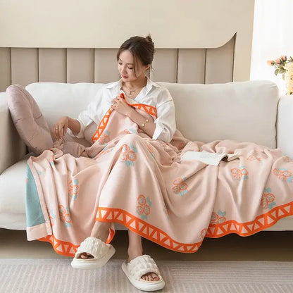 A soft peach summer quilt with orange and blue florals and geometric border draped over a woman made from decorbites bamboo four layer