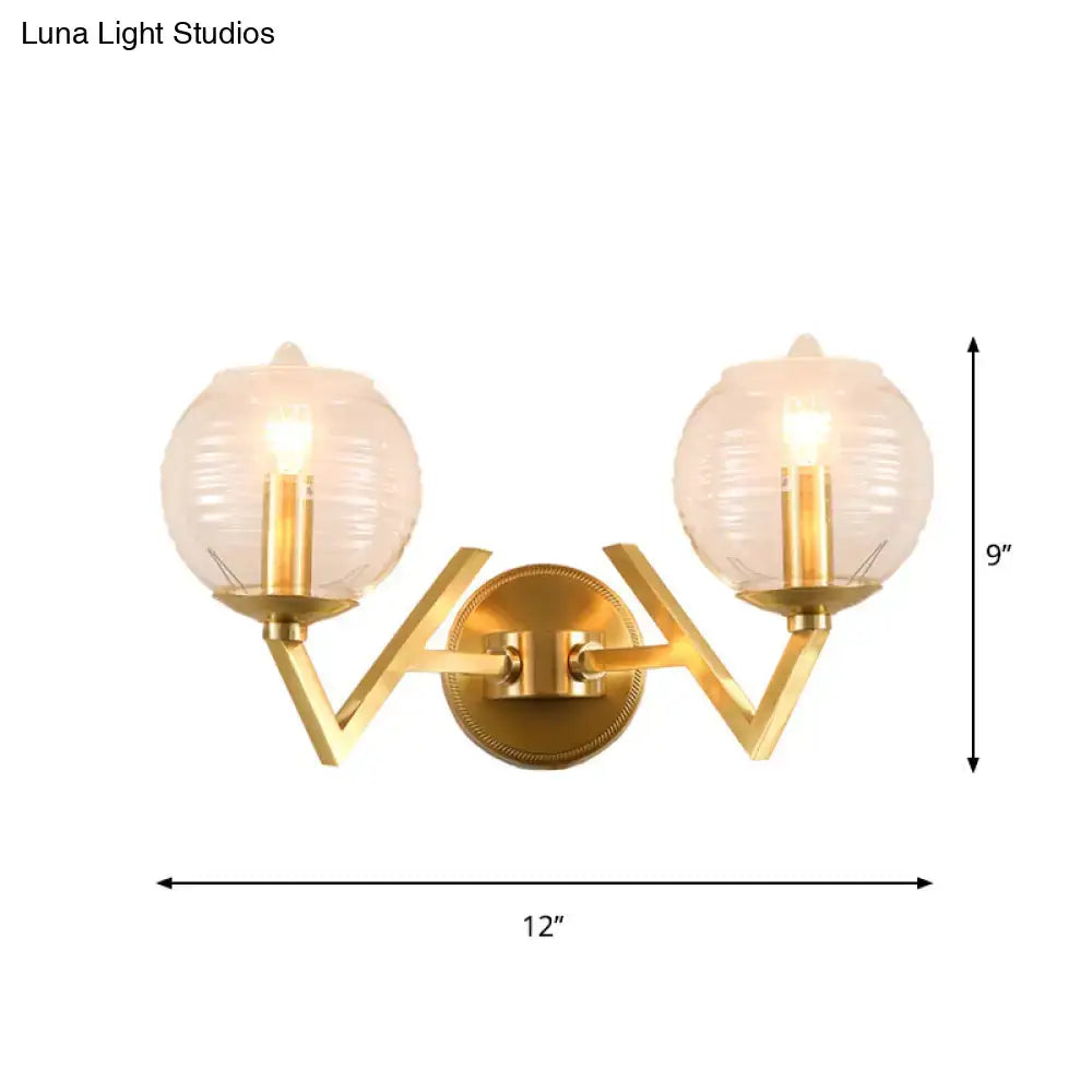 Brass ball sconce with ribbed glass shade featuring gold finish and geometric v-shaped arm for bedroom wall lighting