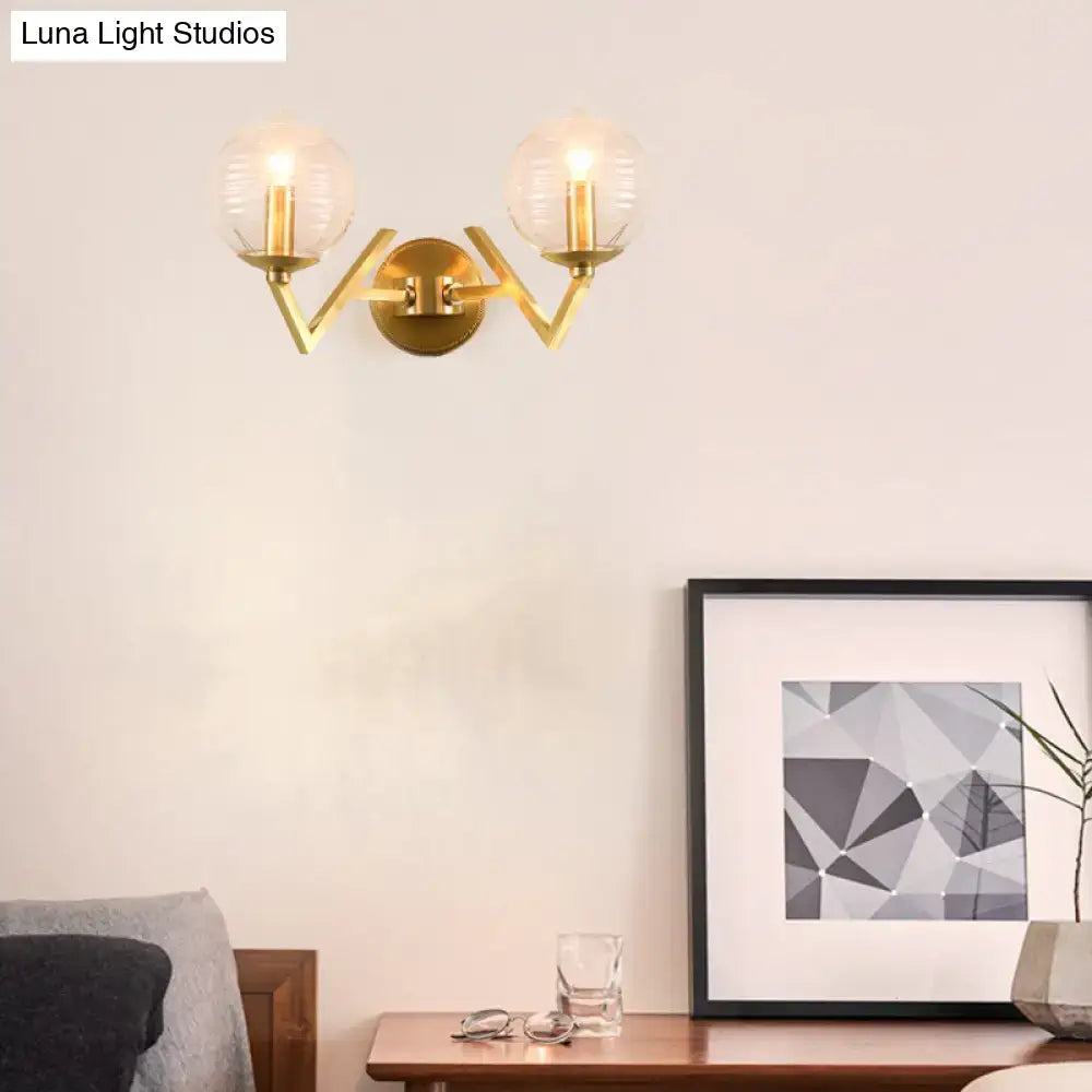 Brass ball sconce with gold-toned geometric arm and two ribbed glass shades for bedroom wall lighting