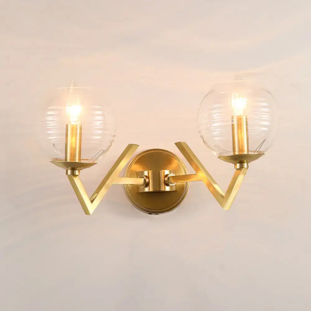 Brass ball sconce with gold-toned angular arms and two clear ribbed glass shades for bedroom wall lighting