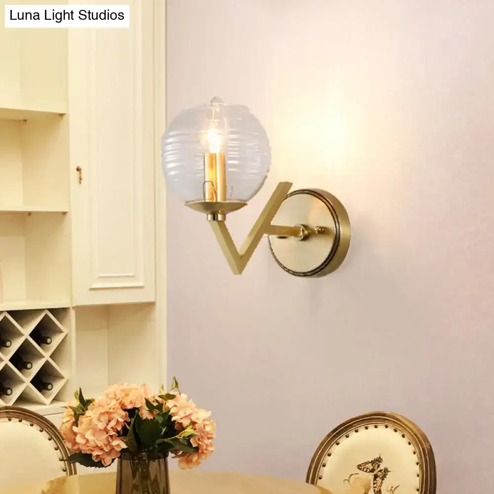 Brass ball sconce with ribbed glass shade and exposed filament bulb for bedroom wall lighting in gold tone