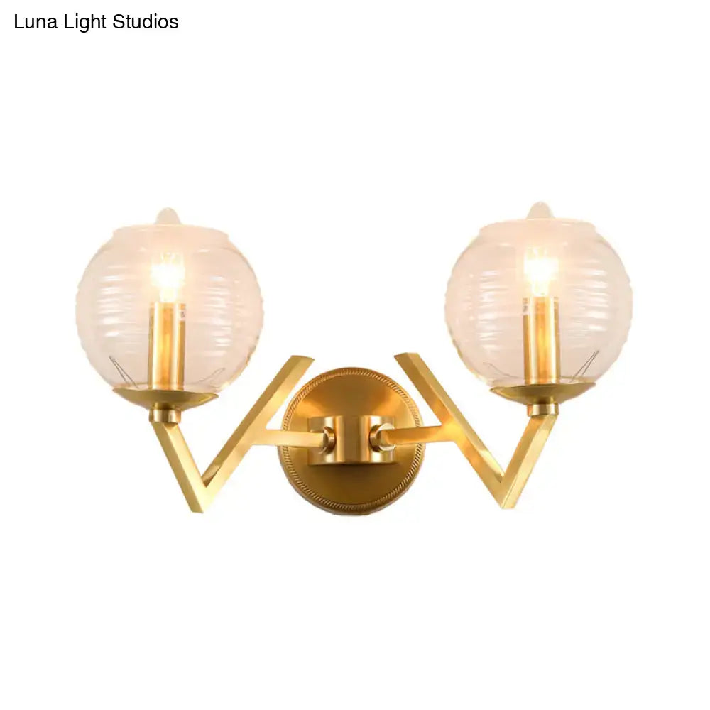 Brass ball sconce with ribbed glass shade and gold-toned v-shaped metal frame for bedroom wall lighting