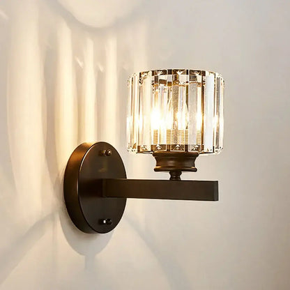 A sleek dark bronze brass decorbites crystal glass wall sconce with a cylindrical faceted crystal glass shade for bedroom lighting