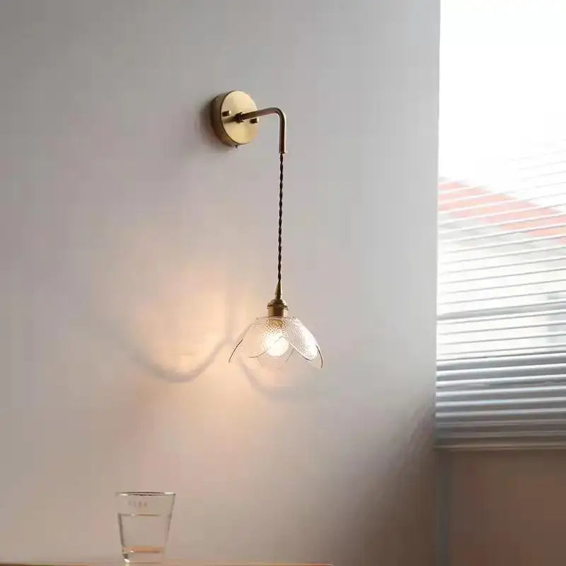 A delicate brass wall lamp with a twisted cord and gray petal-shaped glass led shade for bathroom use