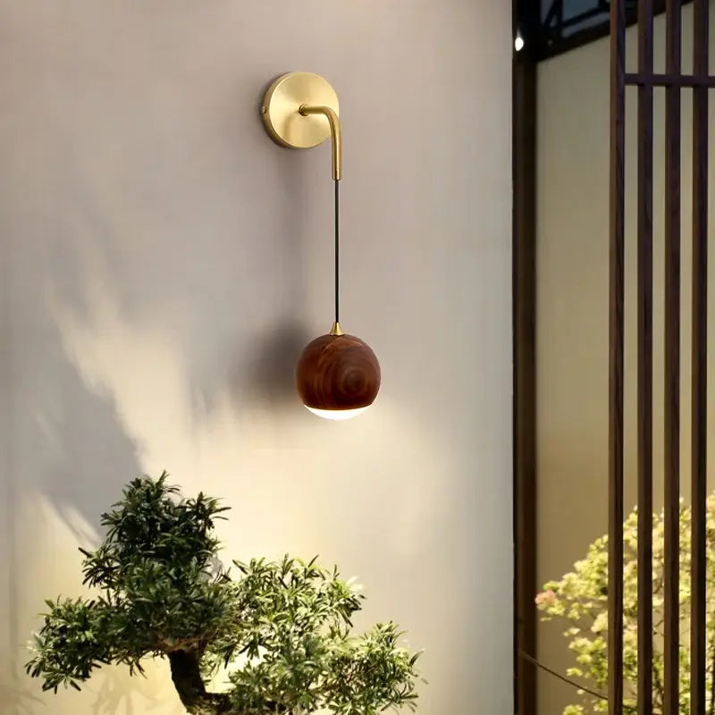 A sleek brass wall lamp with led walnut wood spherical shade by decorbites emitting soft ambient light