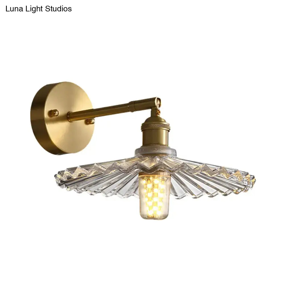 Brass scalloped bedside sconce light fixture with faceted clear glass shade and exposed led bulb for bedroom use
