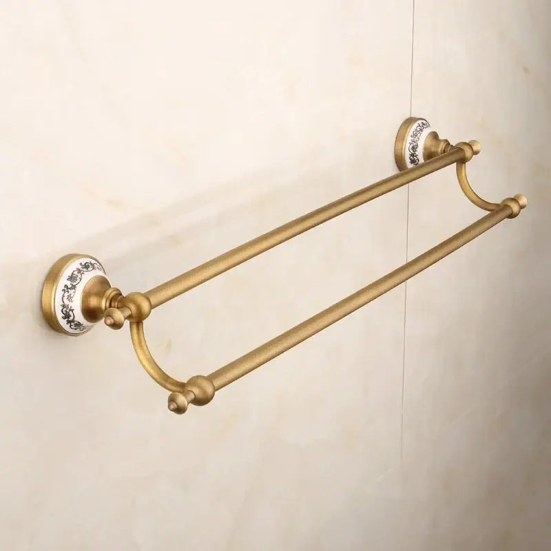 Antique brass double towel rack with ornate white ceramic end caps and black floral detail in decorbites bronze bathroom hardware set
