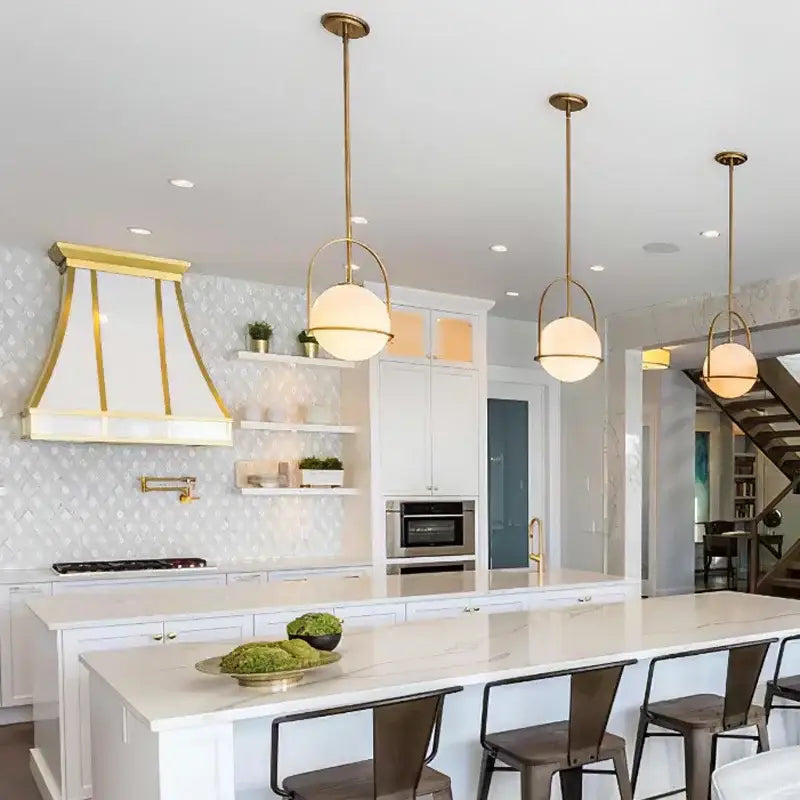 Three elegant brushed brass glass ball ceiling lights with frosted glass shades above a modern kitchen island