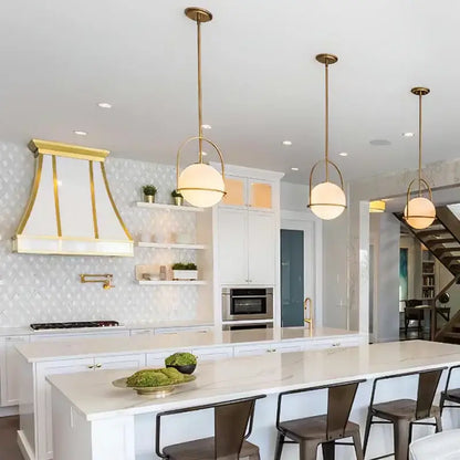 Three elegant brushed brass glass ball ceiling lights with frosted glass shades above a modern kitchen island