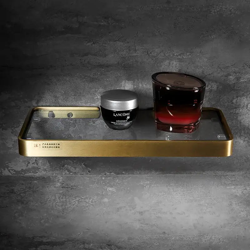 Brushed gold and black corner shelf with glass frame holding lancôme skincare jar and dark red gradient candle decorbites brushed gold bathroom storage organizer