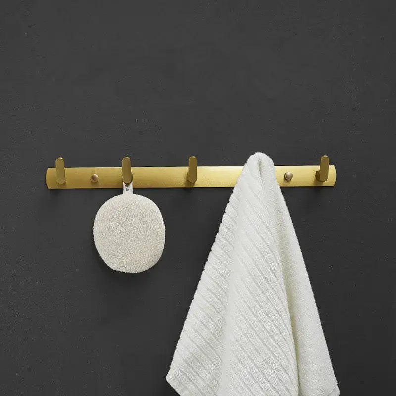 Brushed gold metal robe hooks with five hooks holding white textured sponge and ribbed towel by decorbites