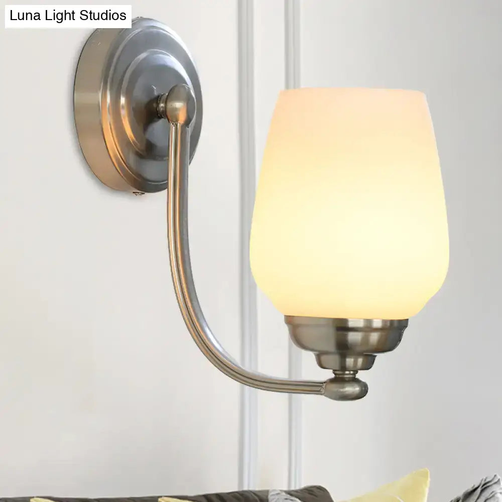 A sleek brushed nickel wall lamp with a curved arm and warm frosted milk glass shade for stairways