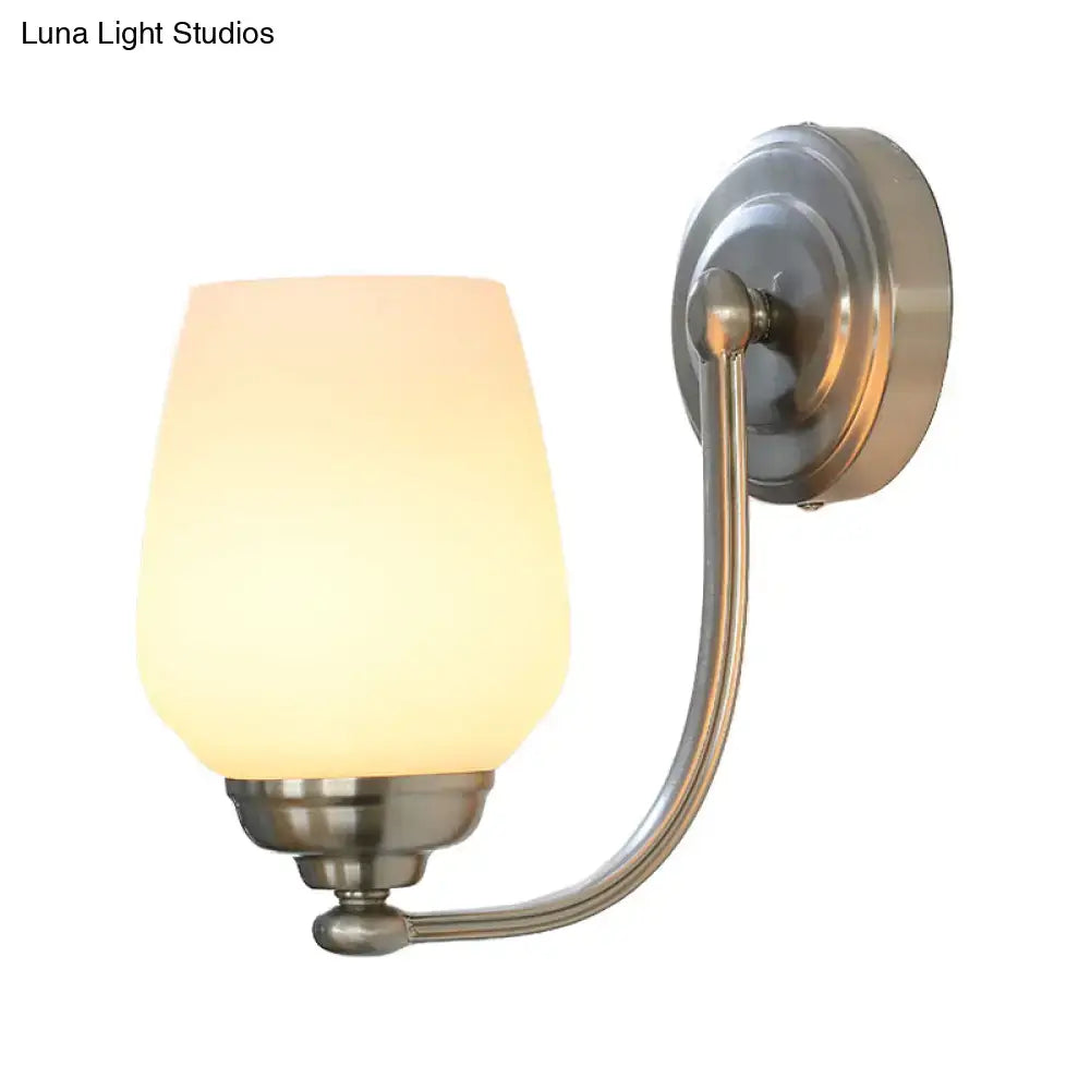 A brushed nickel wall lamp with a warm frosted milk glass shade mounted on a curved stairway sconce