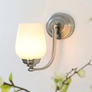 Brushed nickel wall lamp with milk glass shade softly glowing, ideal for stairways and indoor lighting
