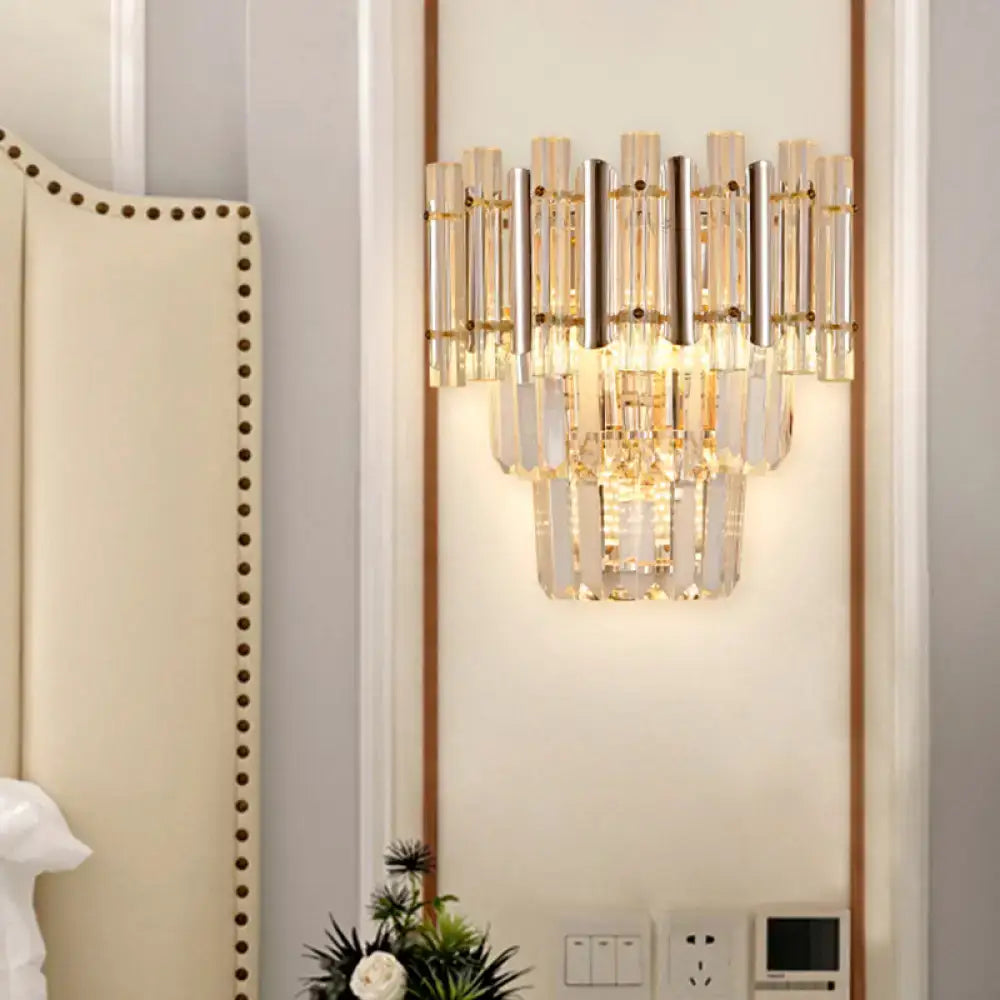 Butterfly tiered gold finish crystal wall sconce with cascading clear prisms and polished metal rods emitting warm glow