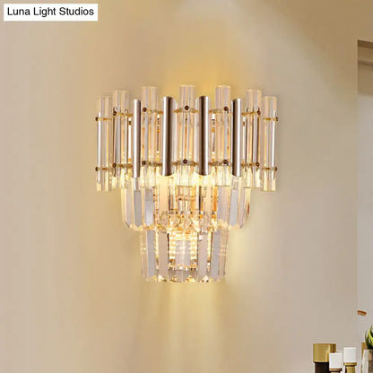 Butterfly tiered gold finish crystal wall sconce with clear tubes and polished gold accents emitting warm bedroom light