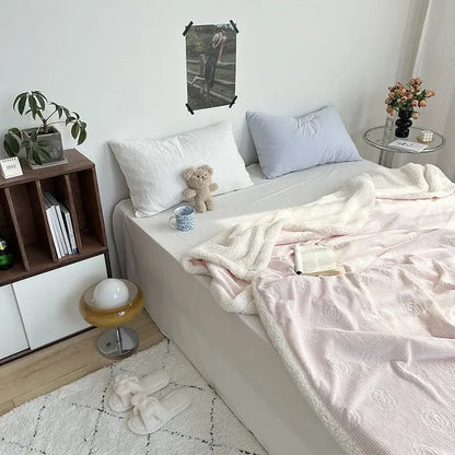Soft pink decorbites camellia jacquard lamb wool cozy blanket with fluffy white border draped over bed