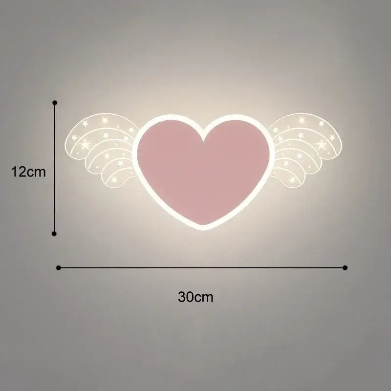 A soft pink heart-shaped cartoon wall lamp with white wings and star patterns illuminated by a warm glow