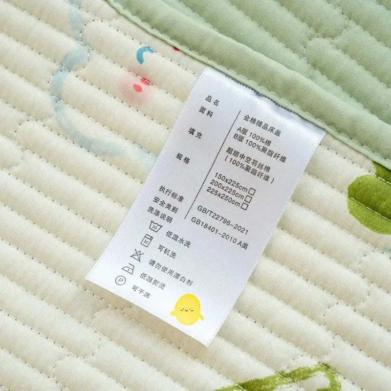 White fabric care label with black chinese text and yellow chick on the back of a green cotton quilted bed cover set