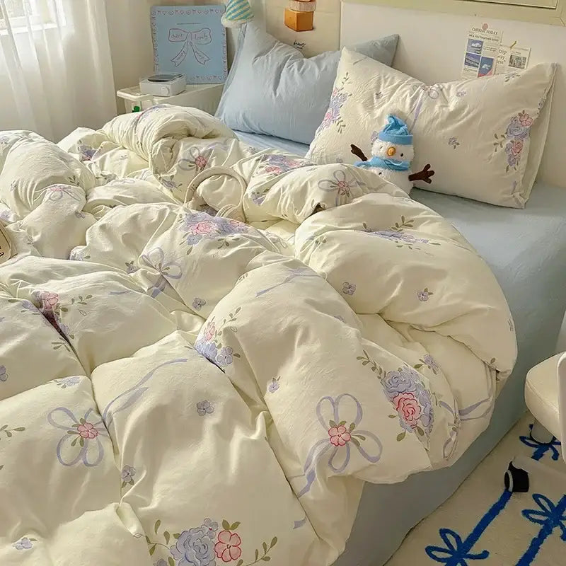 Cream-colored quilted duvet cover with floral and ribbon patterns in soft pink and lavender paired with cotton fitted sheet set