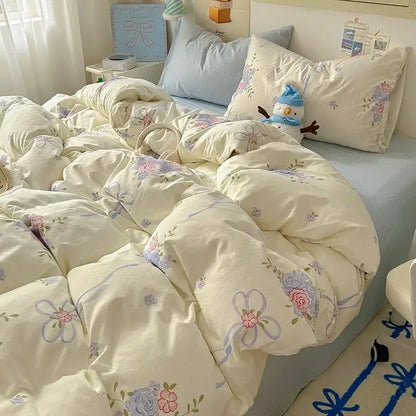 Cream-colored quilted duvet cover with floral and ribbon patterns in soft pink and lavender paired with cotton fitted sheet set