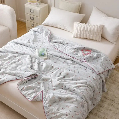 Light blue quilted cooling summer blanket with floral pattern and pink piping for bedroom use