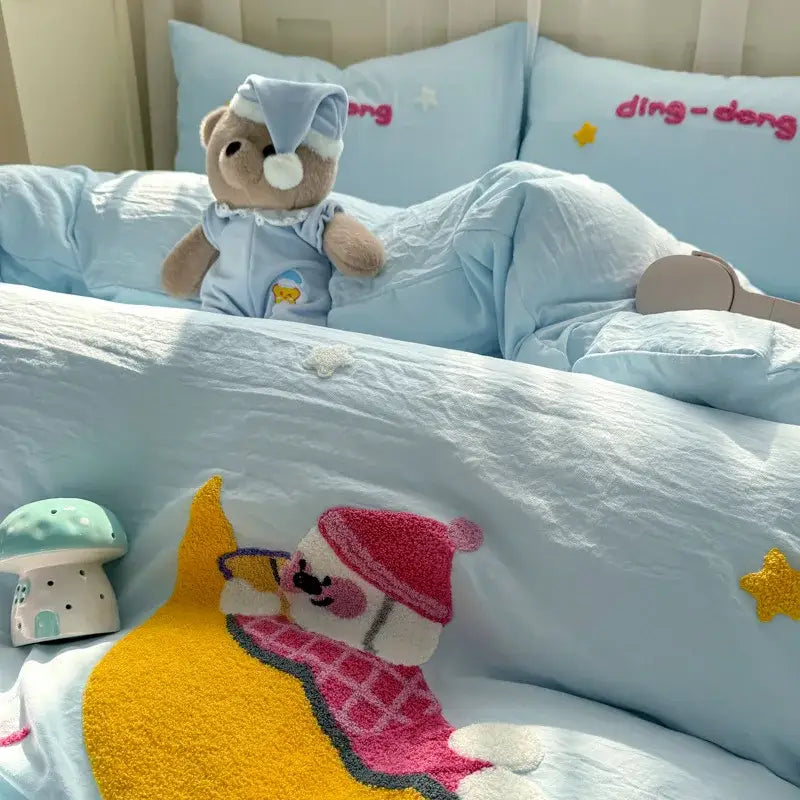 A plush teddy bear with soft brown fur wearing light blue pajama set on a decorbites cartoon towel embroidery bedding set