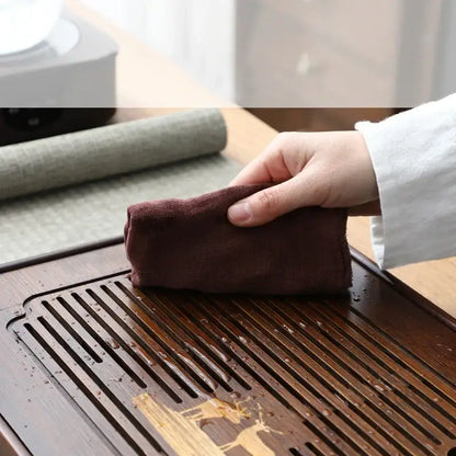 A hand holding a dark brown soft-textured cloth used with a carved deer bamboo tea tray drainage board